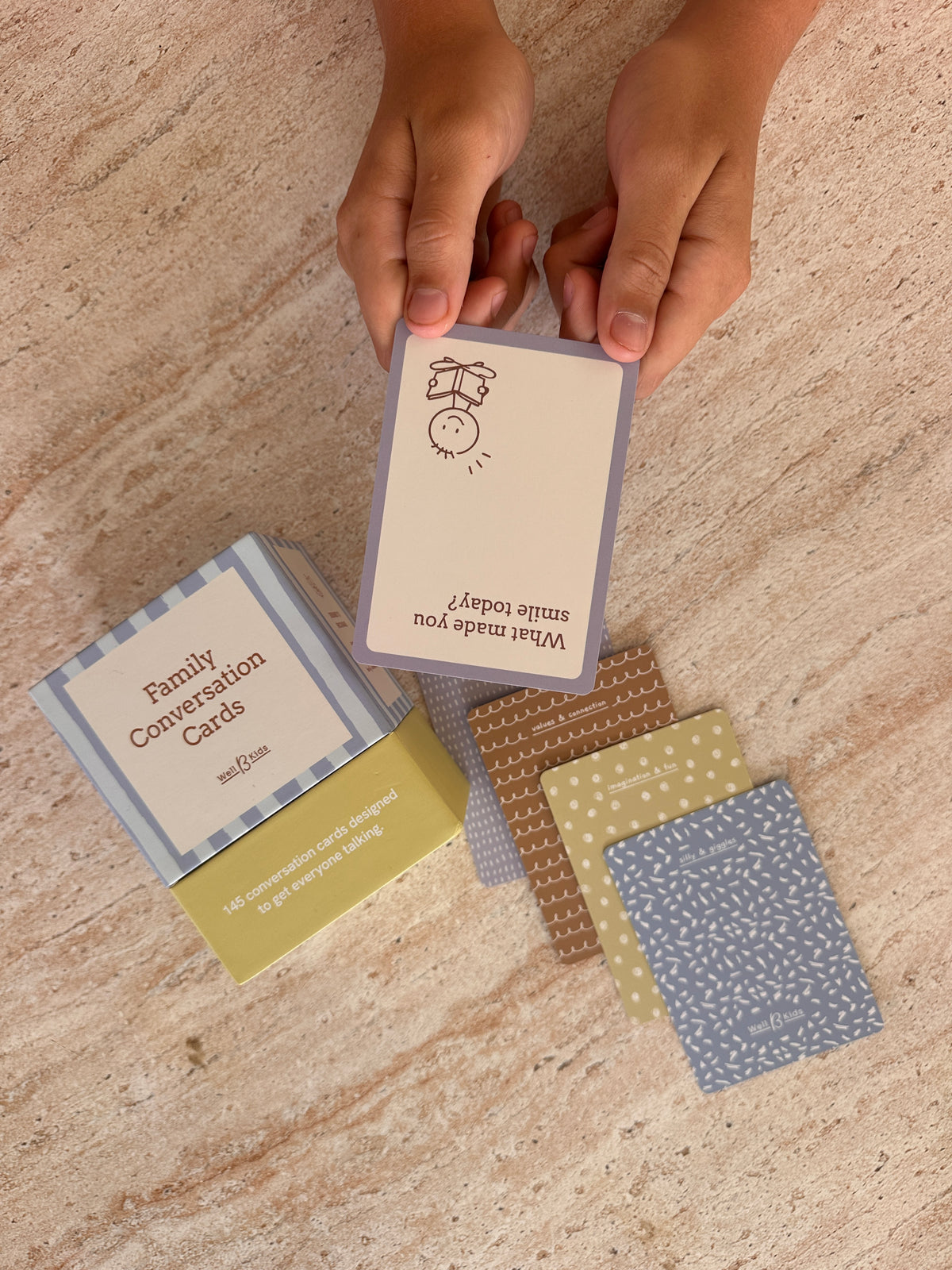 Hands holding a Family Conversation Card above the box, with patterned card backs on the table